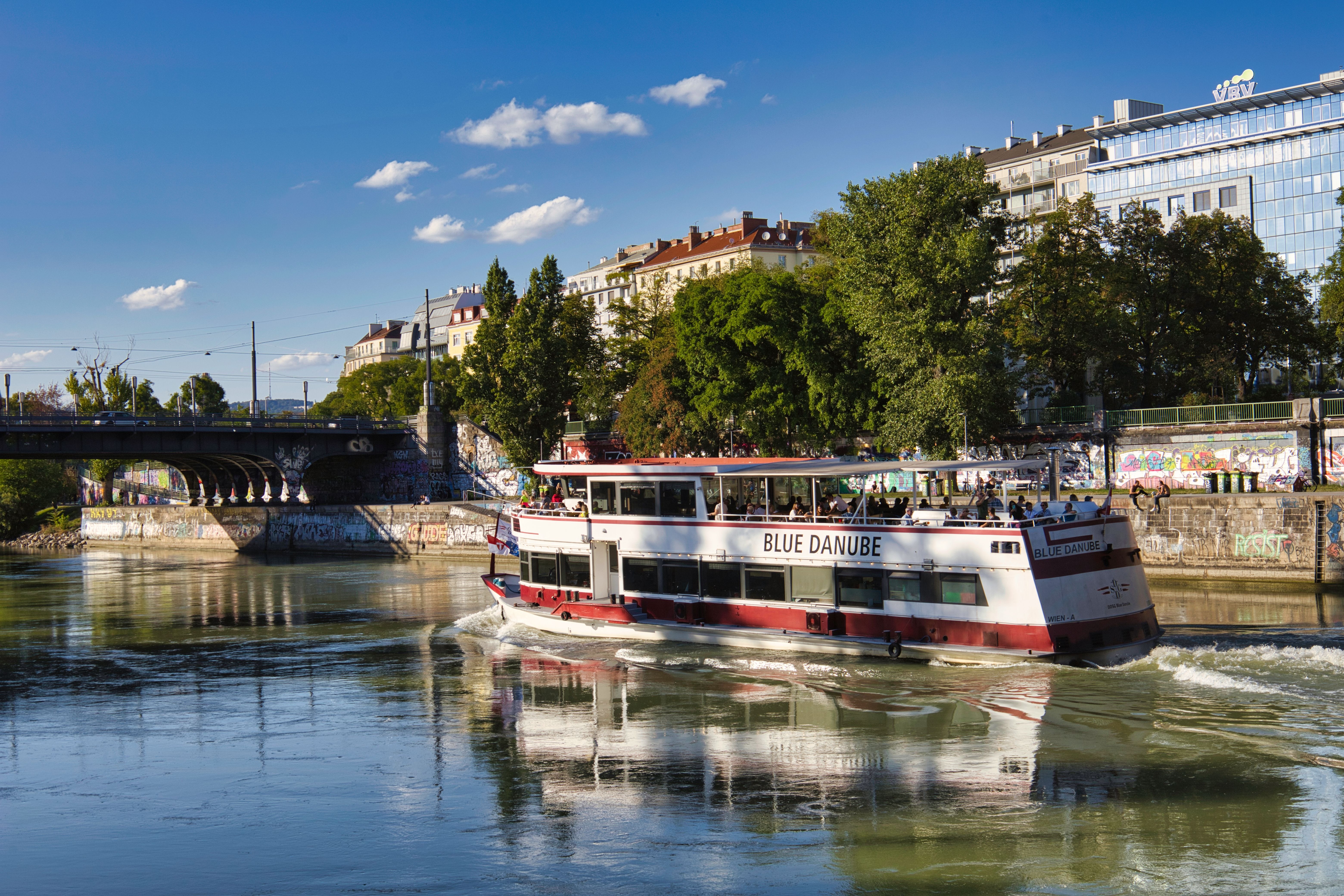 A tourist boat sailing on the Donaukanal on a beautiful summer day with a cityscape of Vienna behind it